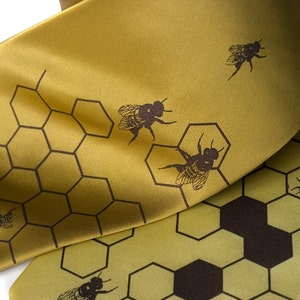Peut inclure: Une cravate en soie dorée avec un motif en nid d'abeille et des silhouettes d'abeilles noires.
