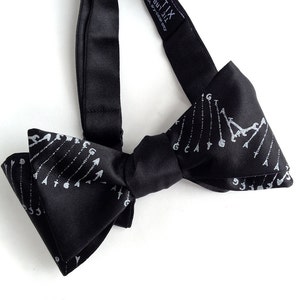 May include: Black bow tie with a white arrow design. The bow tie has silver-coloured text that reads "The X.T.I.X. by Y.C. Collection".