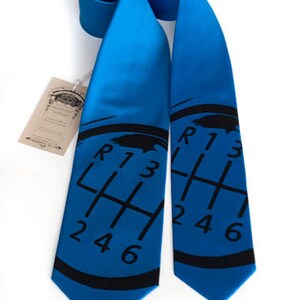 May include: A blue silk tie with a black gear shift pattern printed on it. The gear shift pattern includes the letters R, 1, 2, 3, 4, 5, and 6.