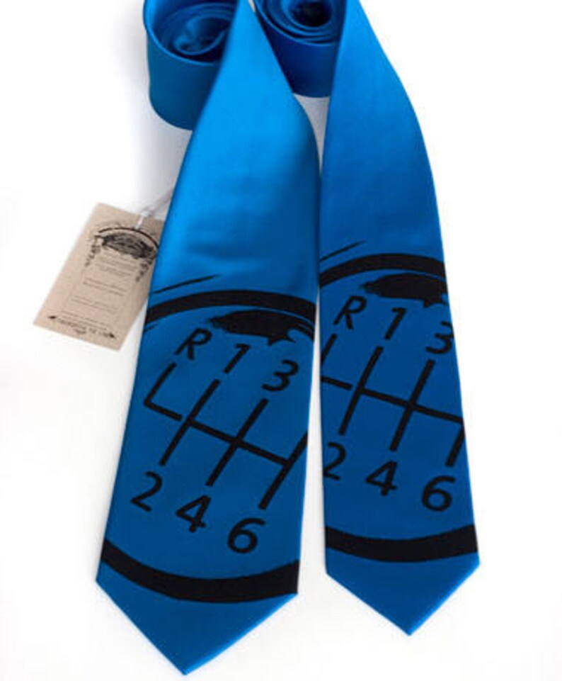 May include: A blue silk tie with a black gear shift pattern printed on it. The gear shift pattern includes the letters R, 1, 2, 3, 4, 5, and 6.