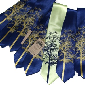 May include: A set of six silk ties featuring a gold tree silhouette design on a navy blue background. One tie is a light green color with a dark silhouette of a tree.