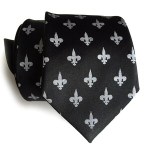 May include: A black silk tie with a repeating pattern of silver fleur-de-lis.