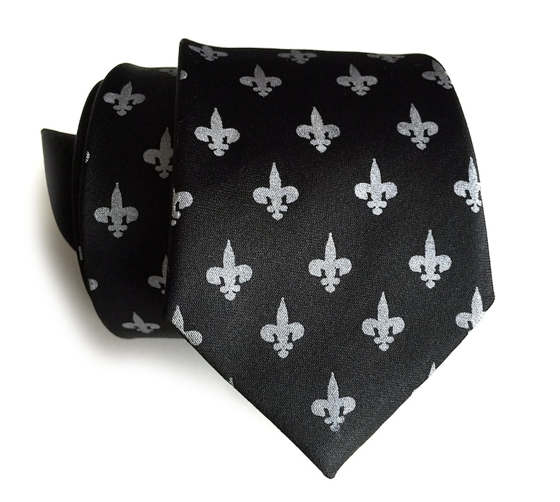 May include: A black silk tie with a repeating pattern of silver fleur-de-lis.