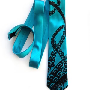 Puede incluir: Una corbata de seda azul turquesa con un dise&ntilde;o de pulpo negro. El pulpo se representa con sus tent&aacute;culos envueltos alrededor de la corbata.