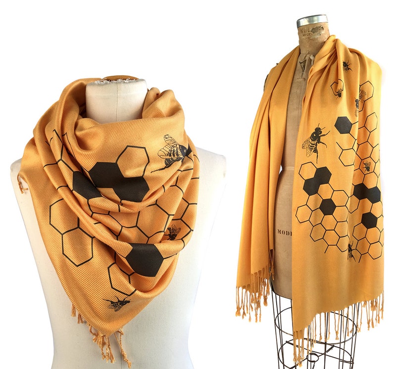 May include: A yellow scarf with a black honeycomb pattern and bee silhouettes. The scarf has fringe on the ends.