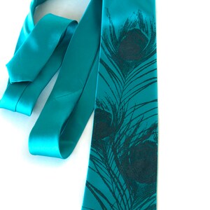 May include: A teal blue satin tie with a black peacock feather print. The tie is tied in a knot and the ends are hanging down.