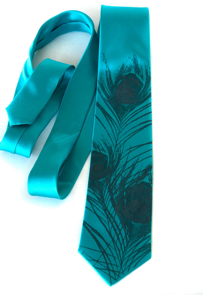 May include: A teal blue satin tie with a black peacock feather print. The tie is tied in a knot and the ends are hanging down.