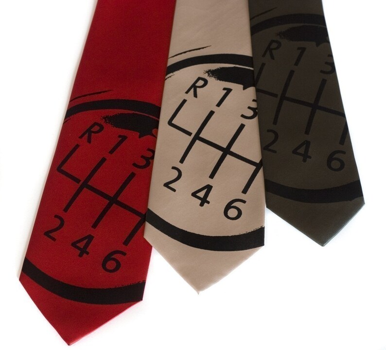 May include: Three silk ties with a black and white gear shift pattern. The ties are red, beige, and dark green.
