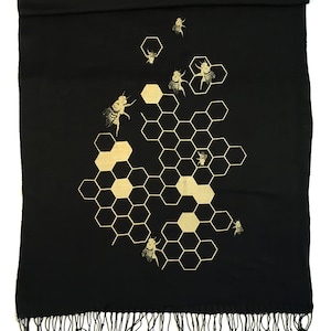 May include: Black scarf with a gold honeycomb pattern and bees. The scarf has a fringe border.