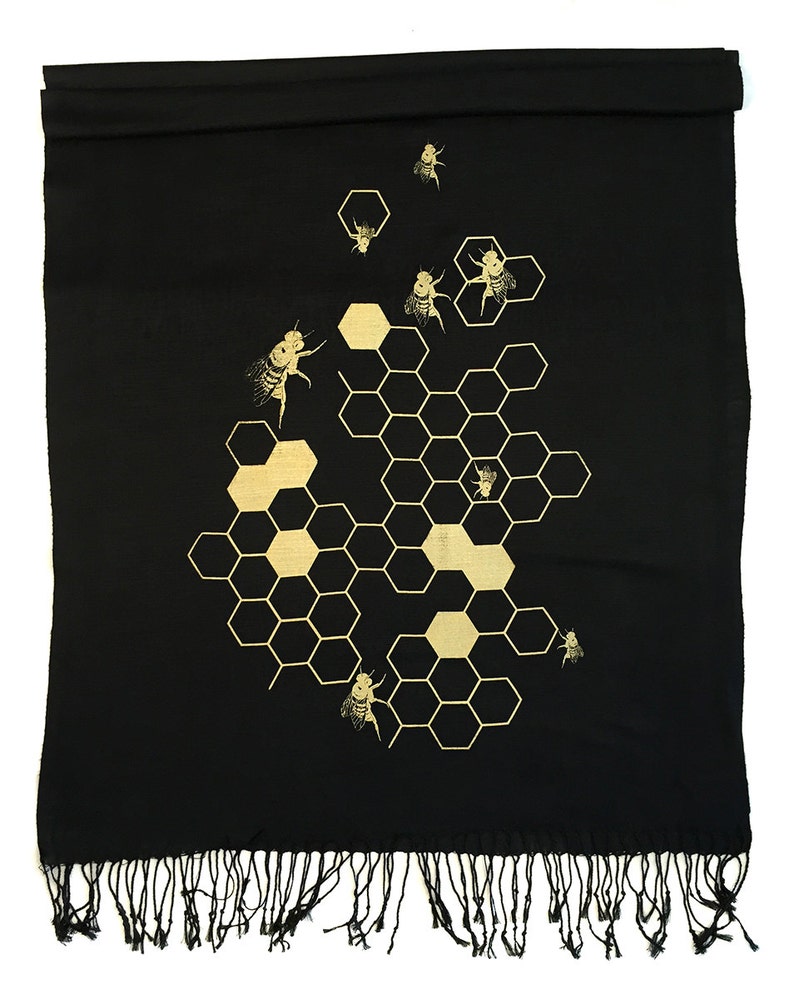 May include: Black scarf with a gold honeycomb pattern and bees. The scarf has a fringe border.