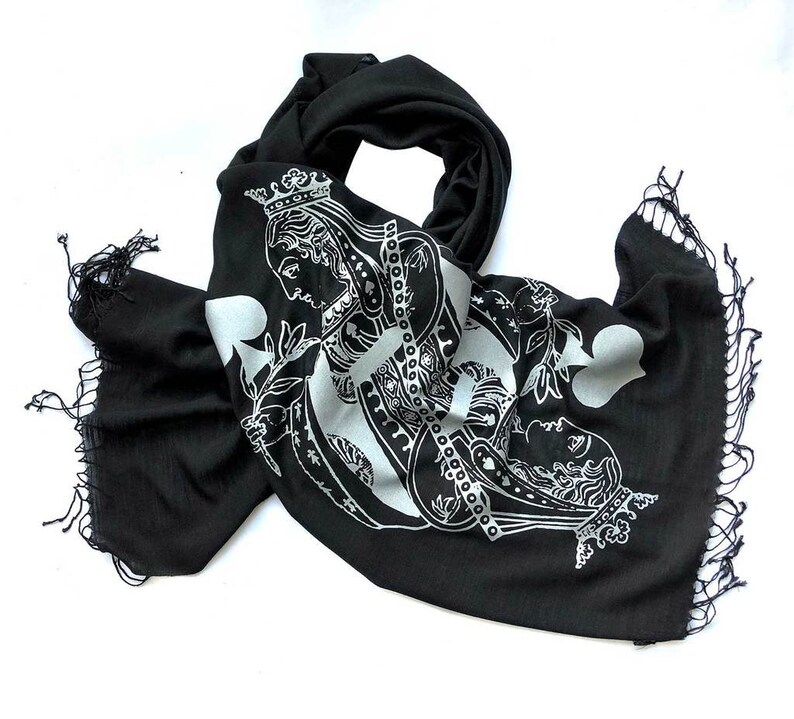 May include: Black scarf with a white print of the Queen of Spades playing card. The scarf has a fringe border.
