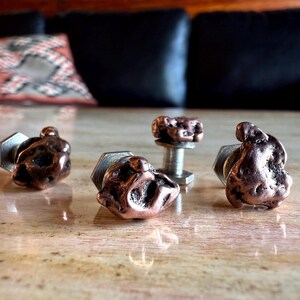May include: Four copper-colored cufflinks and a matching stud. The cufflinks have a textured, organic shape, with a silver-colored, hexagonal backing. The stud has a similar copper-colored, textured top and a silver post.