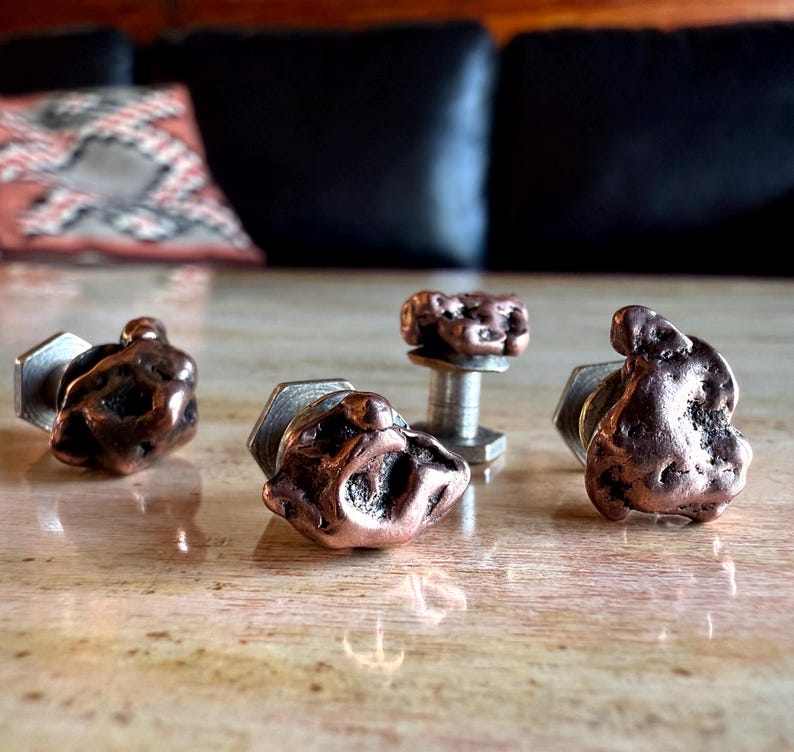 May include: Four copper-colored cufflinks and a matching stud. The cufflinks have a textured, organic shape, with a silver-colored, hexagonal backing. The stud has a similar copper-colored, textured top and a silver post.