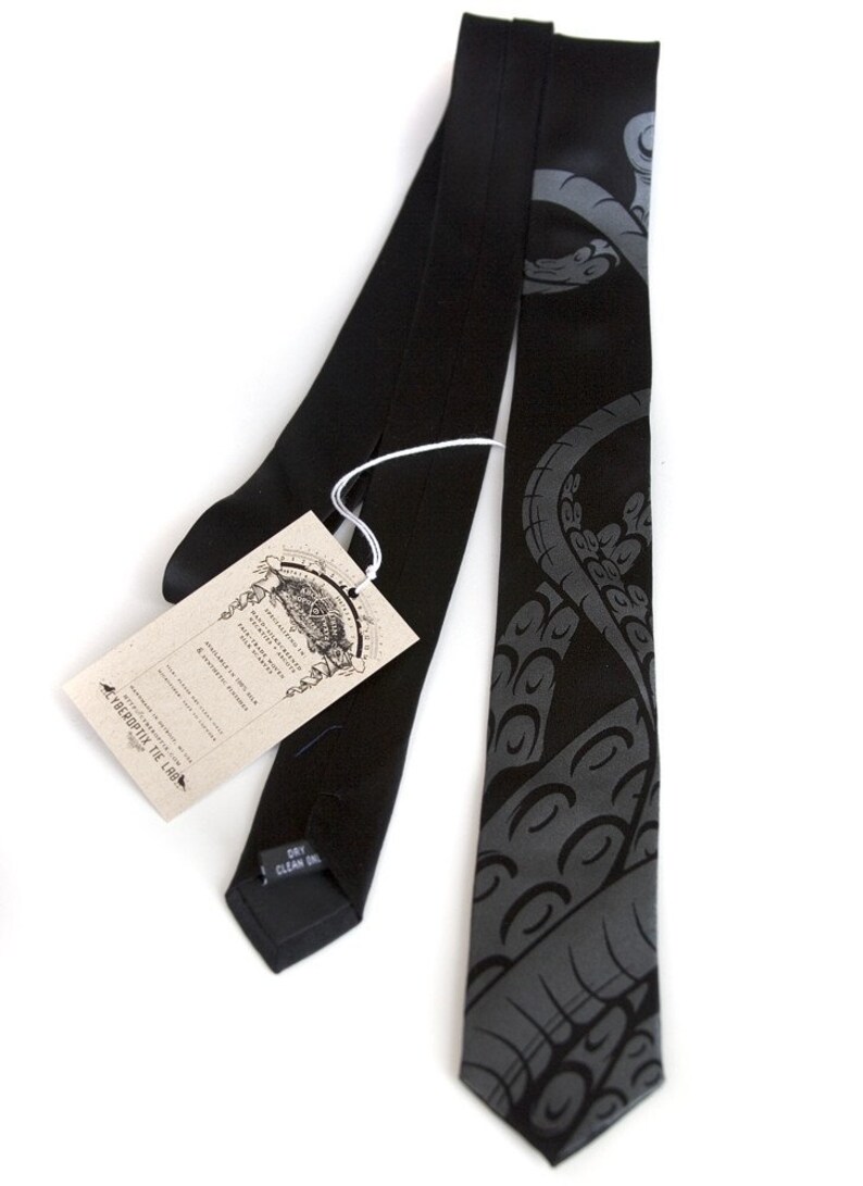 Puede incluir: Una corbata de seda negra con un dise&ntilde;o de pulpo gris. La corbata tiene una etiqueta que dice "The Verbosity Tie Lab" y "Hand Made in the USA".