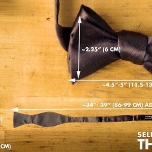 May include: A self-tie, traditional style thistle bow tie in black satin. The bow tie measures approximately 2.5 inches wide and 4.5 to 5 inches long. The tie is adjustable and measures 34 to 39 inches in length.
