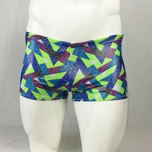 May include: A pair of colorful swim trunks with a geometric pattern. The trunks feature a vibrant design of blue, green, purple, and silver shapes. The shorts are displayed on a white mannequin.