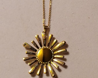 Puede incluir: Un collar de oro con un colgante de sol. El colgante está hecho de metal y tiene una superficie texturizada.