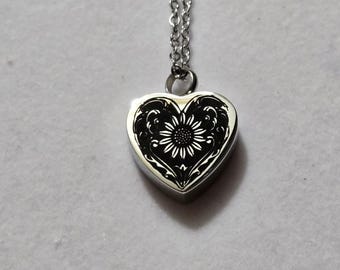 May include: A silver-toned heart-shaped pendant necklace featuring a black engraved sunflower design with intricate scrollwork details. The pendant hangs from a delicate silver-toned metal chain with small oval links, creating a polished look.