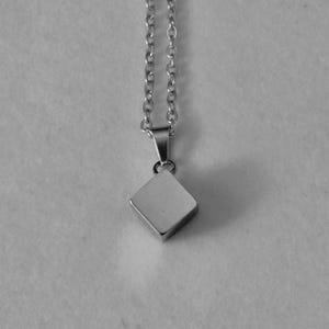 May include: A silver-colored necklace with a square pendant. The pendant is a small, polished square suspended from a delicate chain. The chain and pendant are both made of a shiny, metallic material.