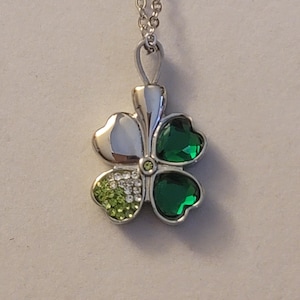 May include: A silver chain necklace with a four-leaf clover pendant. The clover is decorated with green and clear rhinestones.