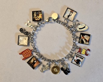 May include: A silver-toned charm bracelet featuring various music-themed pendants, including square photo charms, a red military-style jacket, a white fedora, a gold record, a rhinestone-encrusted glove, musical notes, and the letters ABC.