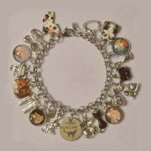 May include: A silver-toned charm bracelet featuring various cat-themed pendants, including colorful enamel cat faces, round glass cabochons with cat portraits, and a circular metal tag engraved with the text 'crazy cat lady' and a cat silhouette.