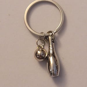 May include: A silver key chain with a bowling pin and bowling ball charm. The charms are attached to a silver key ring.