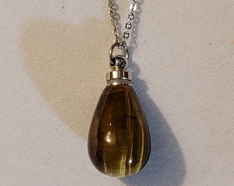 May include: A silver chain necklace with a teardrop-shaped pendant made of tiger's eye stone. The pendant has a metallic silver top.