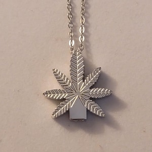 Può includere: Una collana con catena d'argento con un ciondolo a forma di foglia di marijuana d'argento.