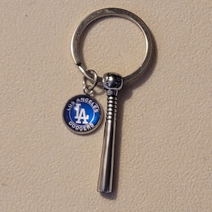 May include: A silver keychain with a Los Angeles Dodgers logo charm and a silver baseball bat charm.