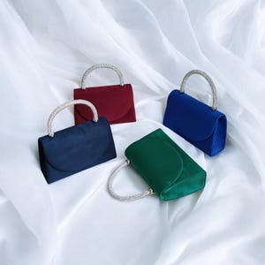 May include: Four small, velvet evening bags with rhinestone handles. The bags are in shades of red, blue, green, and navy.
