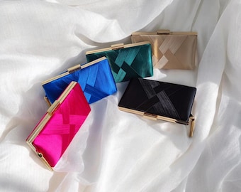 May include: Five different colored satin clutch purses with gold clasps. The clutches are arranged in a row on a white fabric background. The colors are pink, blue, teal, black, and beige.