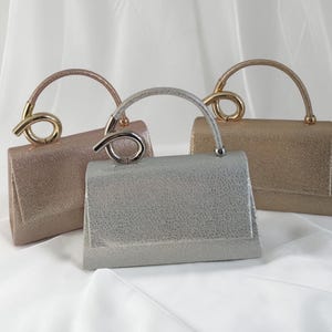 May include: Three glittery handbags in rose gold, silver, and gold. Each bag has a curved handle with a decorative loop. The bags are rectangular with a textured surface, suitable for special events.