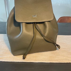 May include: A green leather backpack with a drawstring closure and a silver MK logo.