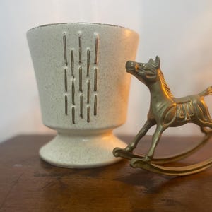 May include: A white ceramic planter with gold accents and a brass rocking horse figurine.