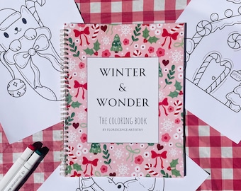 May include: A spiral-bound coloring book titled "Winter & Wonder" with a pink cover featuring a pattern of bows, snowflakes, and greenery. The image includes coloring pages and markers, all set on a red and white checkered surface.