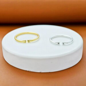 K&ouml;nnte beinhalten: Zwei offene Ringe, einer in Goldoptik und einer in Silberoptik. Der goldene Ring ist an den Enden mit den Buchstaben J und S graviert, w&auml;hrend der silberne Ring an den Enden mit den Buchstaben M und B graviert ist. Beide Ringe sind glatt poliert.