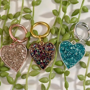 Può includere: Tre ciondoli a forma di cuore con riempimento di glitter. I ciondoli sono in montature oro rosa, oro e argento. I colori dei glitter sono champagne, multicolore e turchese. Ogni ciondolo ha una chiusura abbinata.