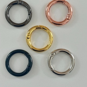Può includere: Un assortimento di cinque anelli tondi con chiusura a molla in metallo di vari colori. I colori includono nero, oro rosa, oro, blu navy e argento. Queste chiusure sono progettate per aprirsi e chiudersi con un meccanismo a molla.