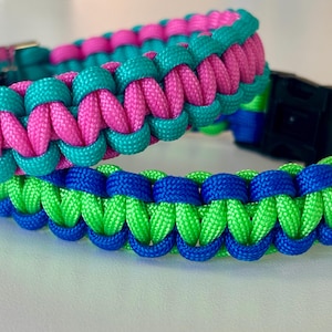 May include: Two paracord collars featuring a braided design. The top collar is woven with bright pink and teal cord, while the bottom collar is woven with vibrant lime green and royal blue cord. Both collars include black plastic side-release buckles.