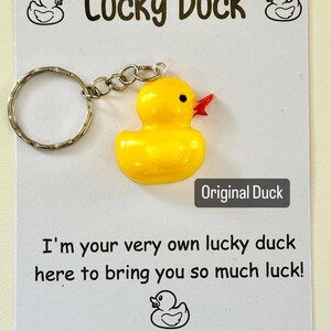 May include: A yellow rubber duck keyring with a red beak and black eyes. The keyring is attached to a silver key ring. The card reads "Lucky Duck" and "I'm your very own lucky duck here to bring you so much luck!" with a small rubber duck illustration at the bottom. The card also includes the text "What The Floof Resin Creations @whatt_hefloof".