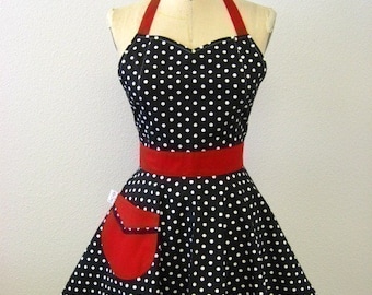 May include: A black and white polka dot apron with a red waistband and a red pocket. The apron has a sweetheart neckline and adjustable straps.