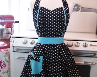 May include: A black and white polka dot apron with a turquoise blue trim and a turquoise blue pocket. The apron has a sweetheart neckline and a full skirt.