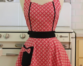 May include: A red and white patterned apron with a black bow and a black waistband. The apron has a black pocket with a white bow on the front.