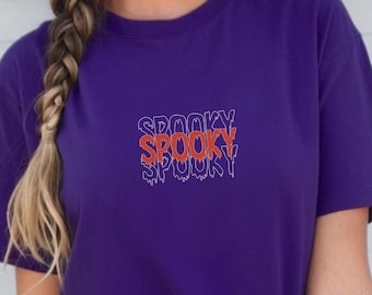 May include: A purple t-shirt with the word "SPOOKY" in a dripping font design. The word is in red with a white outline and the word is repeated three times. The word "PURPLE" is printed in a purple font in the upper right corner.