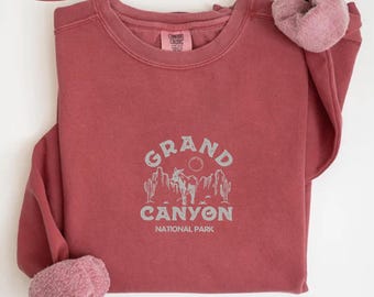 May include: A crimson red sweatshirt with a white graphic design that says "GRAND CANYON NATIONAL PARK" with a silhouette of a donkey and cacti.