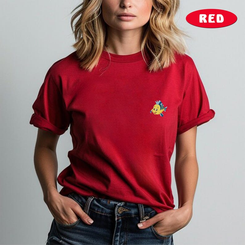 May include: Red t-shirt with a small, embroidered cartoon fish on the chest. The shirt has short sleeves and is made of a soft material. The word "RED" is in a red oval in the top right corner.