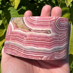 May include: A large, pink and white banded slab of polished pink calcite. The calcite has a swirling, layered pattern.