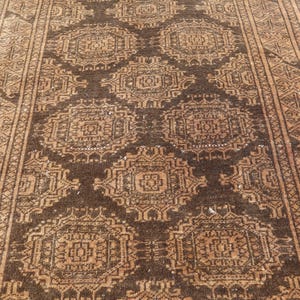 May include: A rectangular, brown and tan rug with an intricate geometric pattern. The rug features repeating square and diamond shapes in varying shades of brown and tan, with a detailed border. The rug's design is symmetrical and traditional.