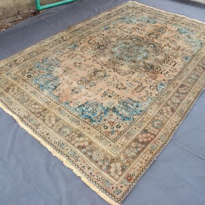 May include: An antique area rug with a central medallion design. The rug features a beige field with blue and brown accents, and a detailed border. The rug has a distressed, vintage appearance.